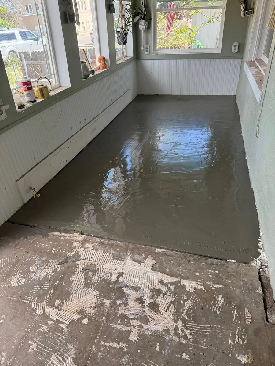 Freshly poured gray concrete floor in a narrow enclosed porch or sunroom with windows on both sides.