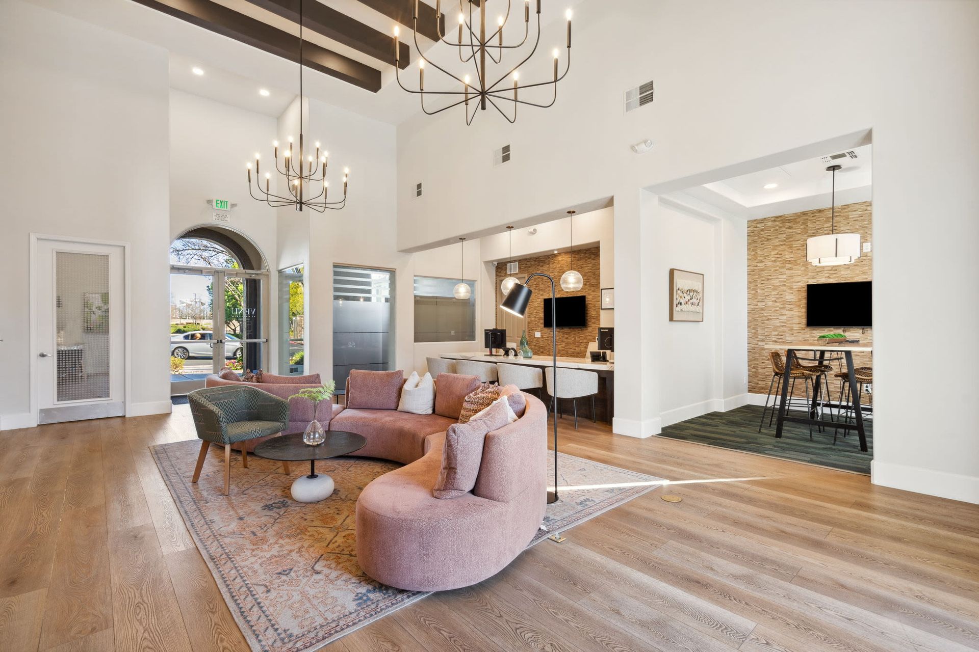 Bright modern community lounge with curved pink sofa, rug, and hanging chandeliers.