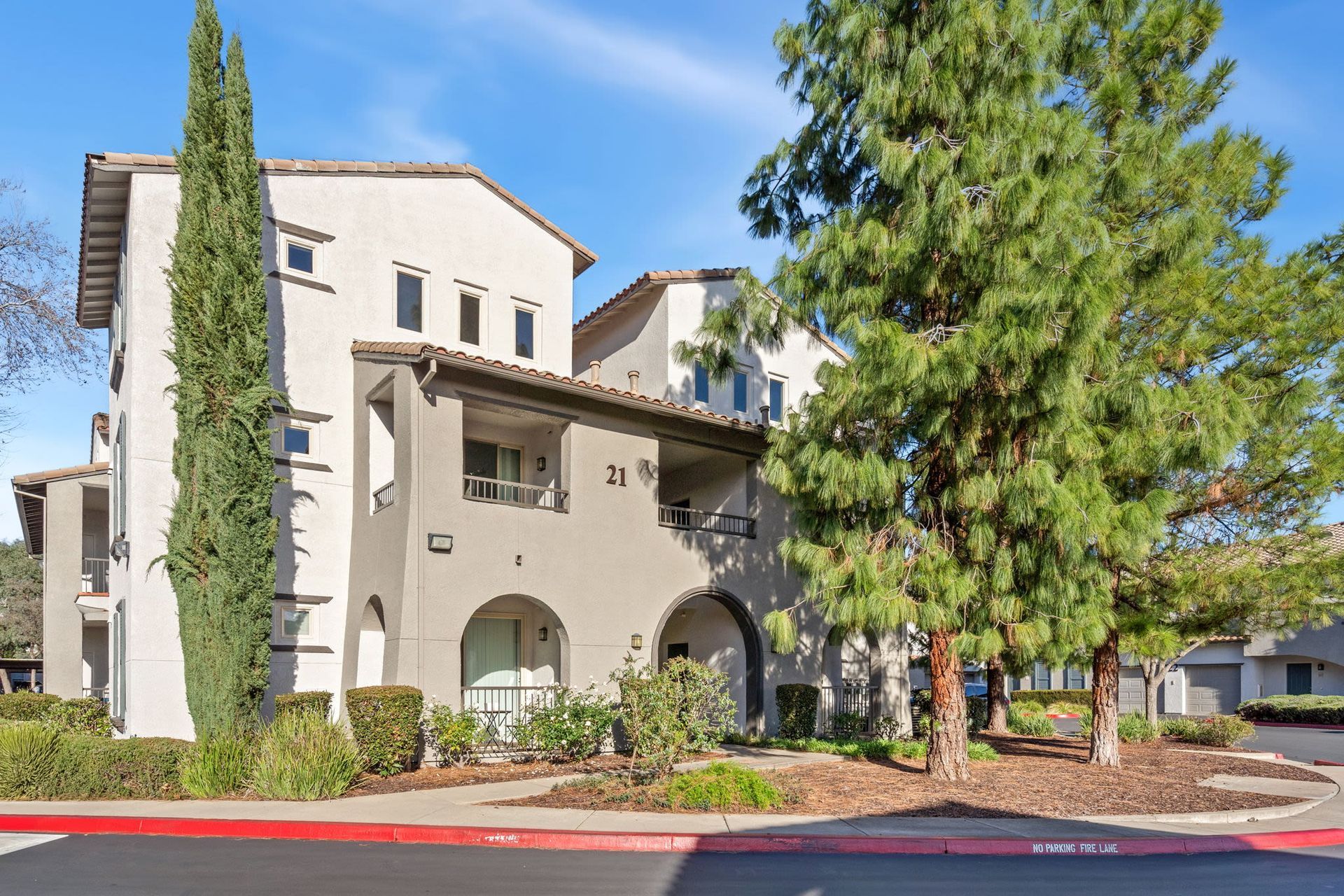 Exterior view of a beige apartment building with landscaping and tall trees.