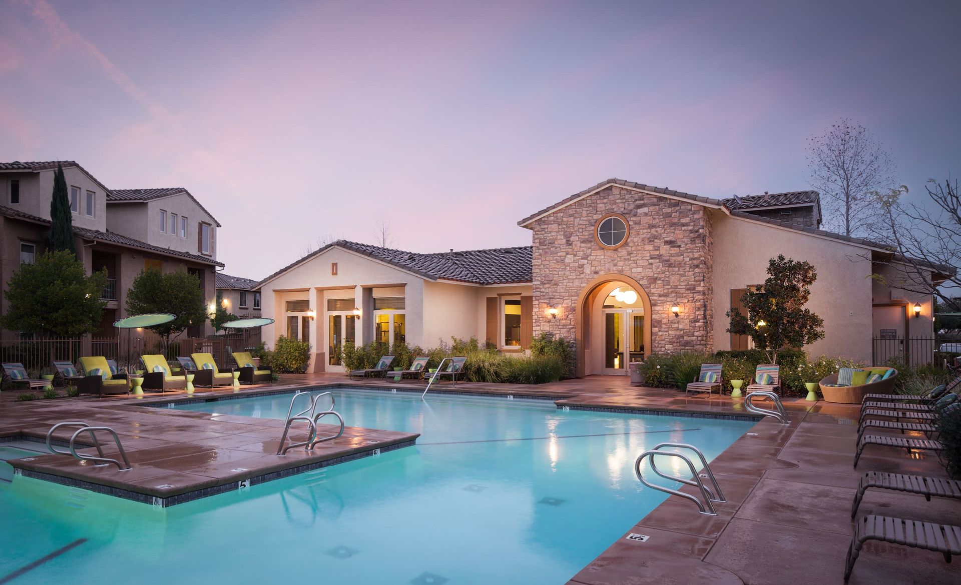 Outdoor pool area at a multifamily community with lounge chairs and a clubhouse.