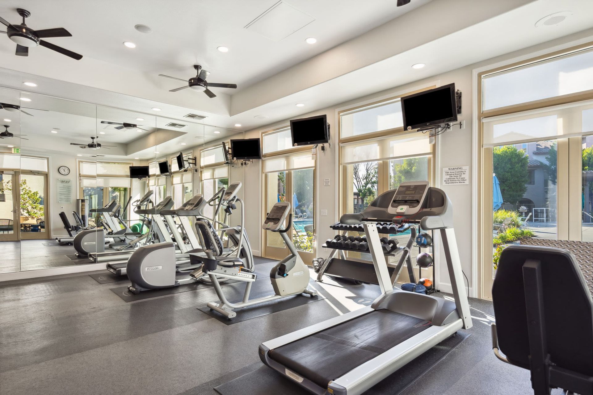 Interior fitness center with cardio machines, mirrors, and wall-mounted TVs.