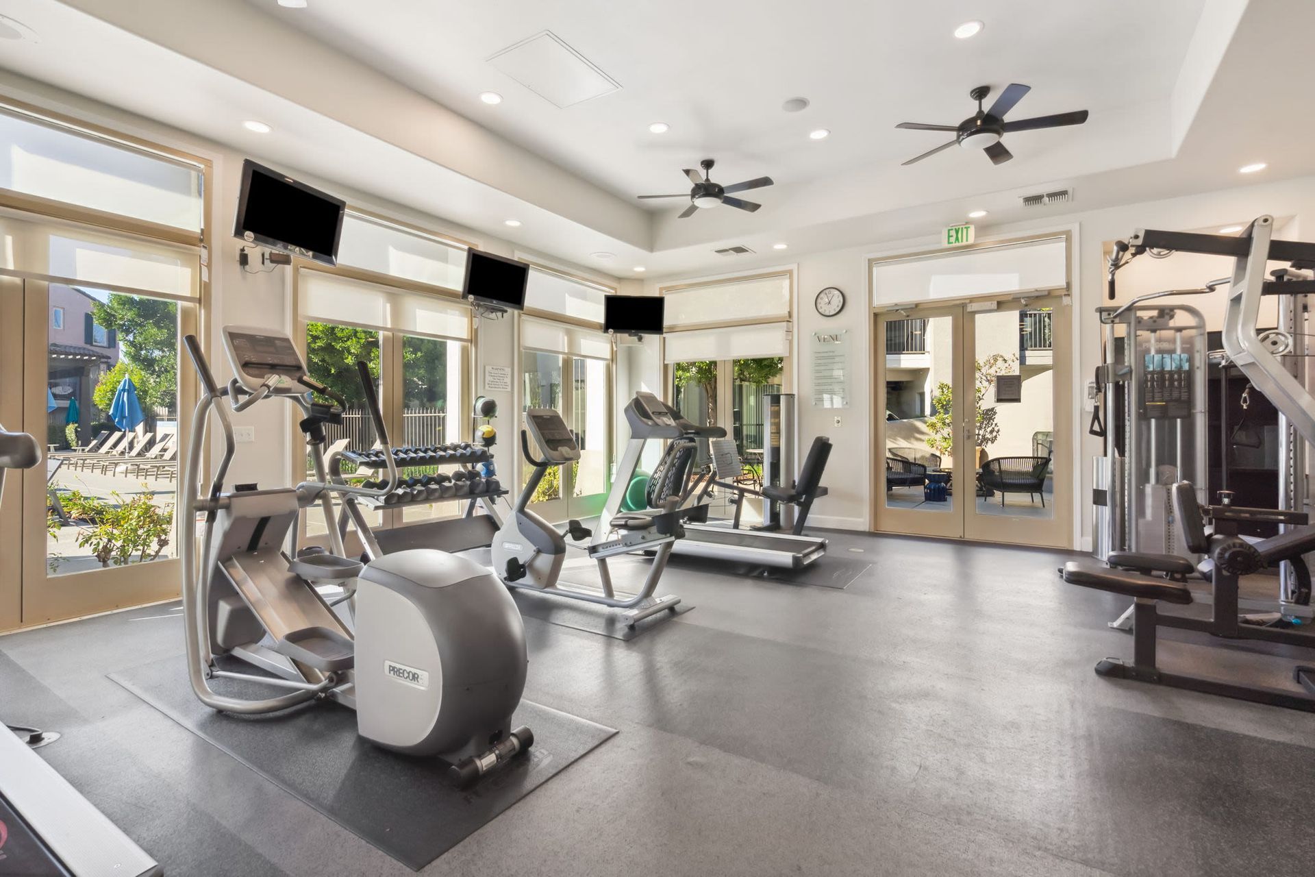 Bright fitness center with cardio machines and weight racks beside large windows.
