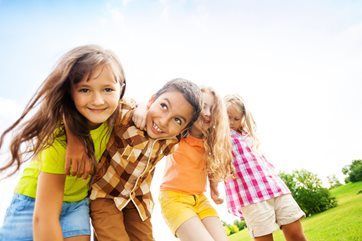 Three children smiling and leaning together outdoors in a sunny grassy field