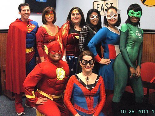 Group of people in superhero costumes posing indoors, including Superman, The Flash, Spider-Man, and Green Lantern.