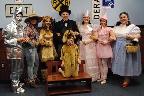 Costumed group posing indoors, including a silver robot, cowboy, bee, princess, and cat characters.
