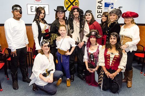 Costumed group posing indoors in pirate-themed outfits with a railroad crossing sign backdrop