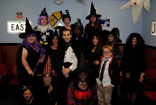 Group of people in Halloween costumes posing indoors in front of a blue wall