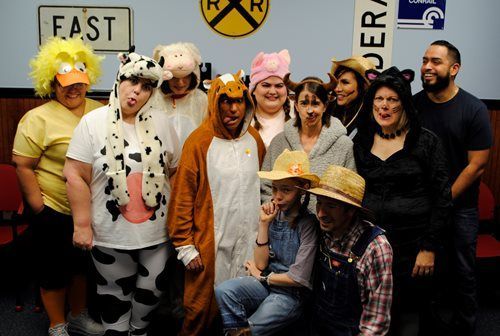 Group of people in costumes posing indoors against a wall with railroad signs and a cow figure.