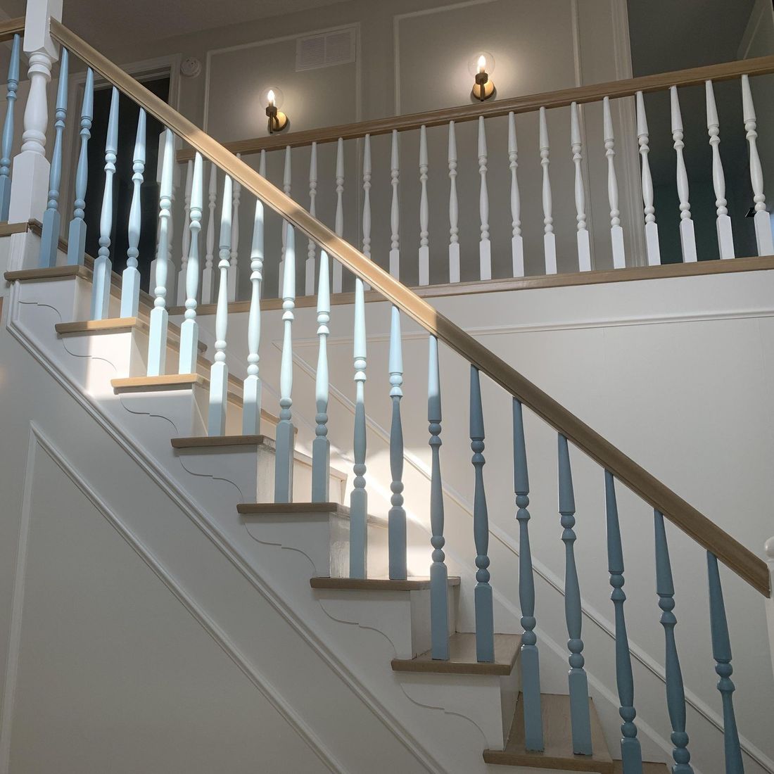 A wooden staircase featuring white handrails and light blue vertical spindles against a white wall with wall molding.