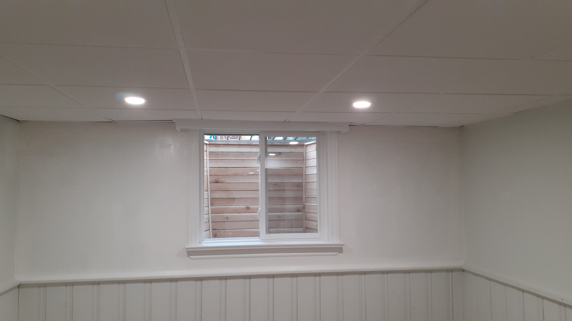 White basement room with recessed lights and a small window above wainscoting.