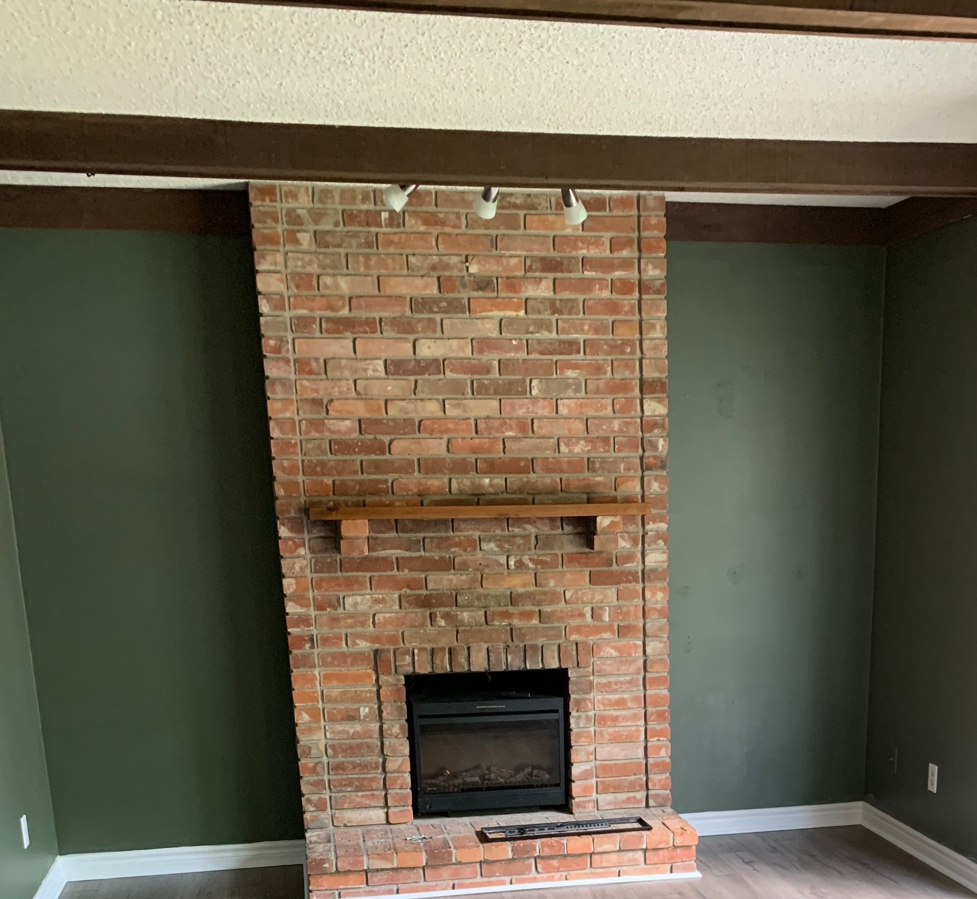 Brick fireplace with dark green walls and a wooden mantel in a living room