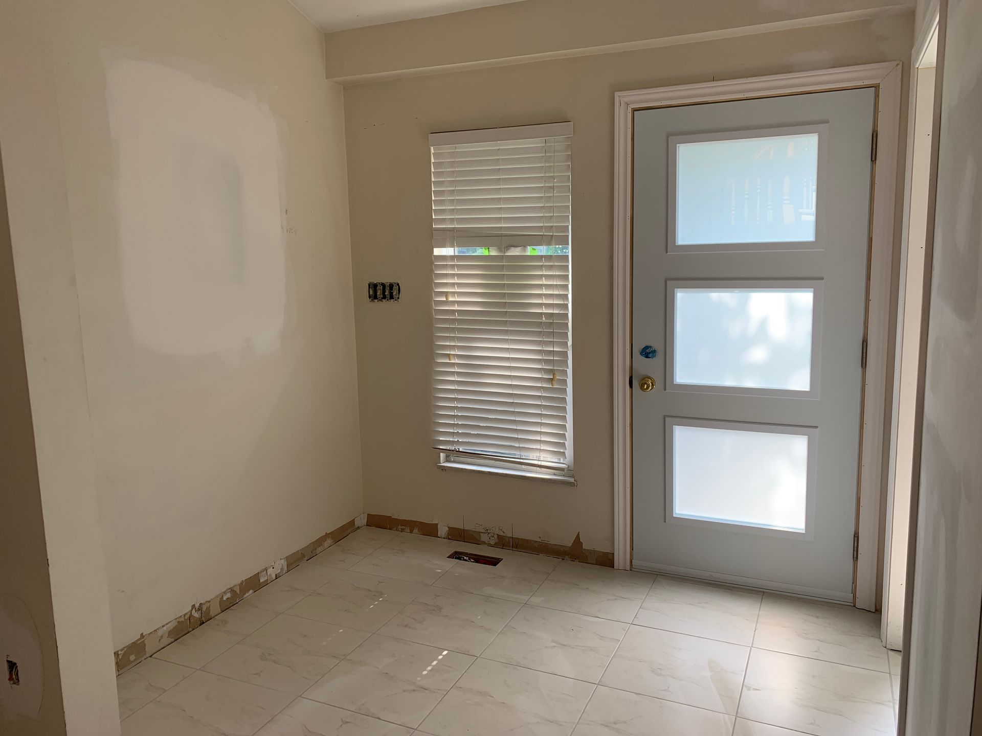 Empty beige room with tiled floor, window blinds, and a door with frosted glass panels
