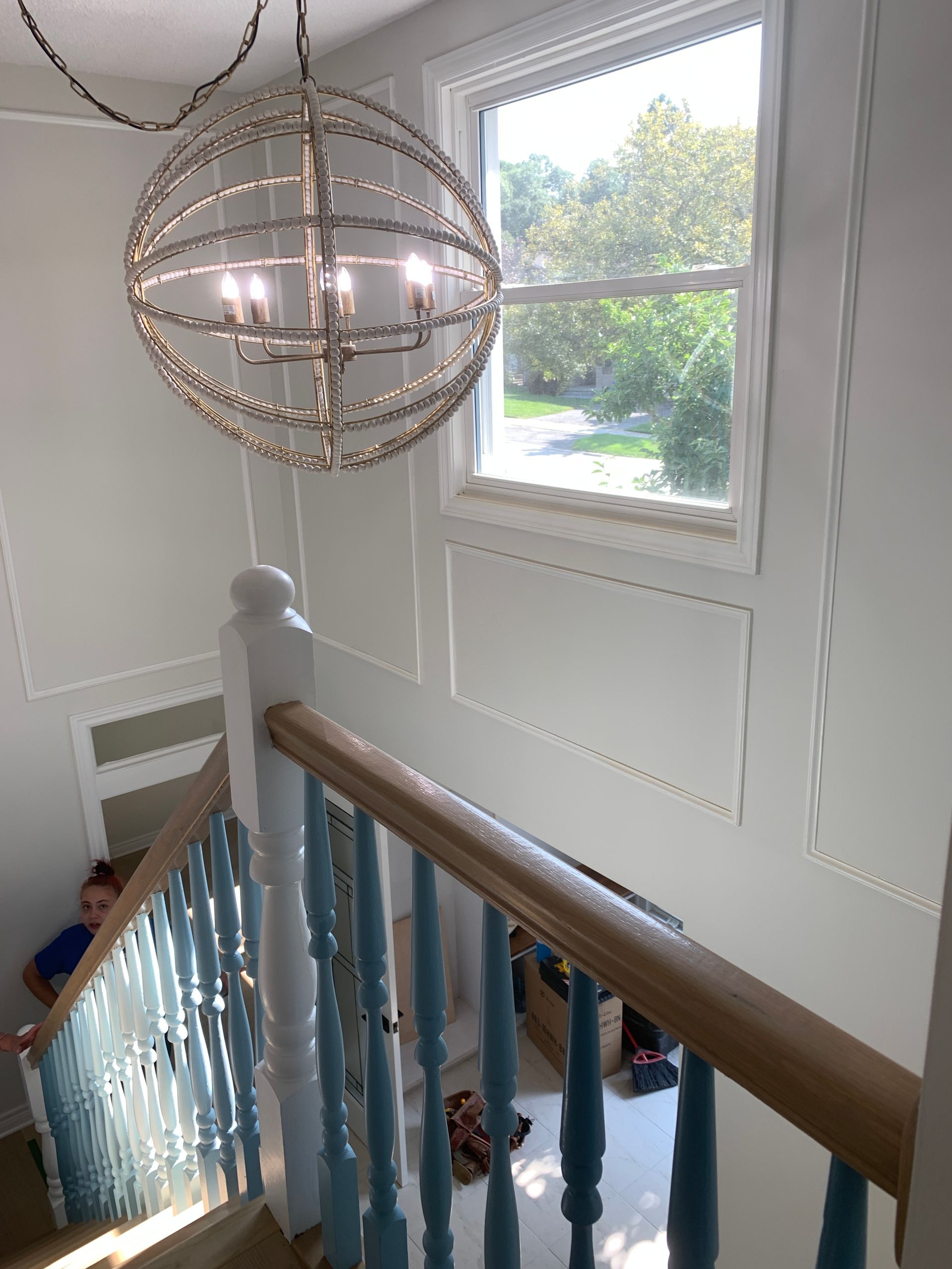 Staircase landing with white walls, wooden railing, and a large spherical chandelier by a bright window
