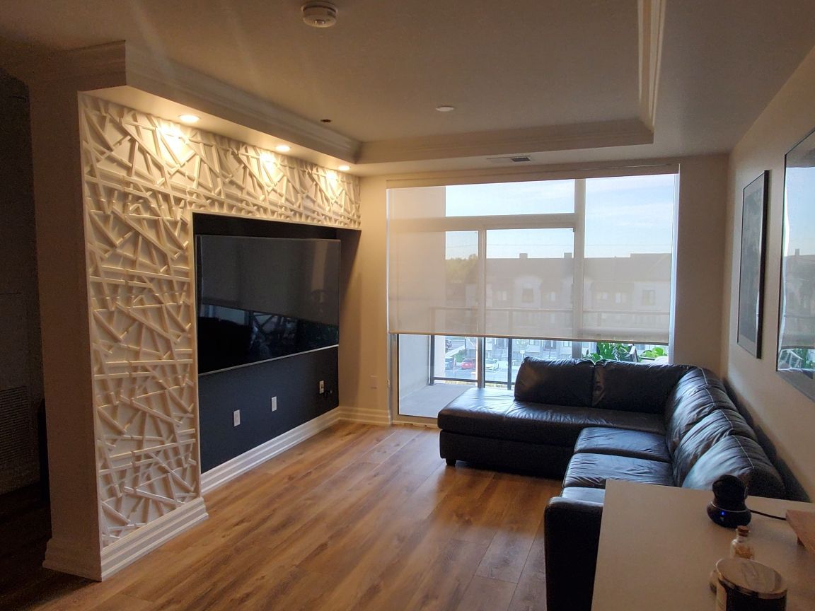 Modern living room with wall-mounted TV, black sectional sofa, and large windows overlooking a city view