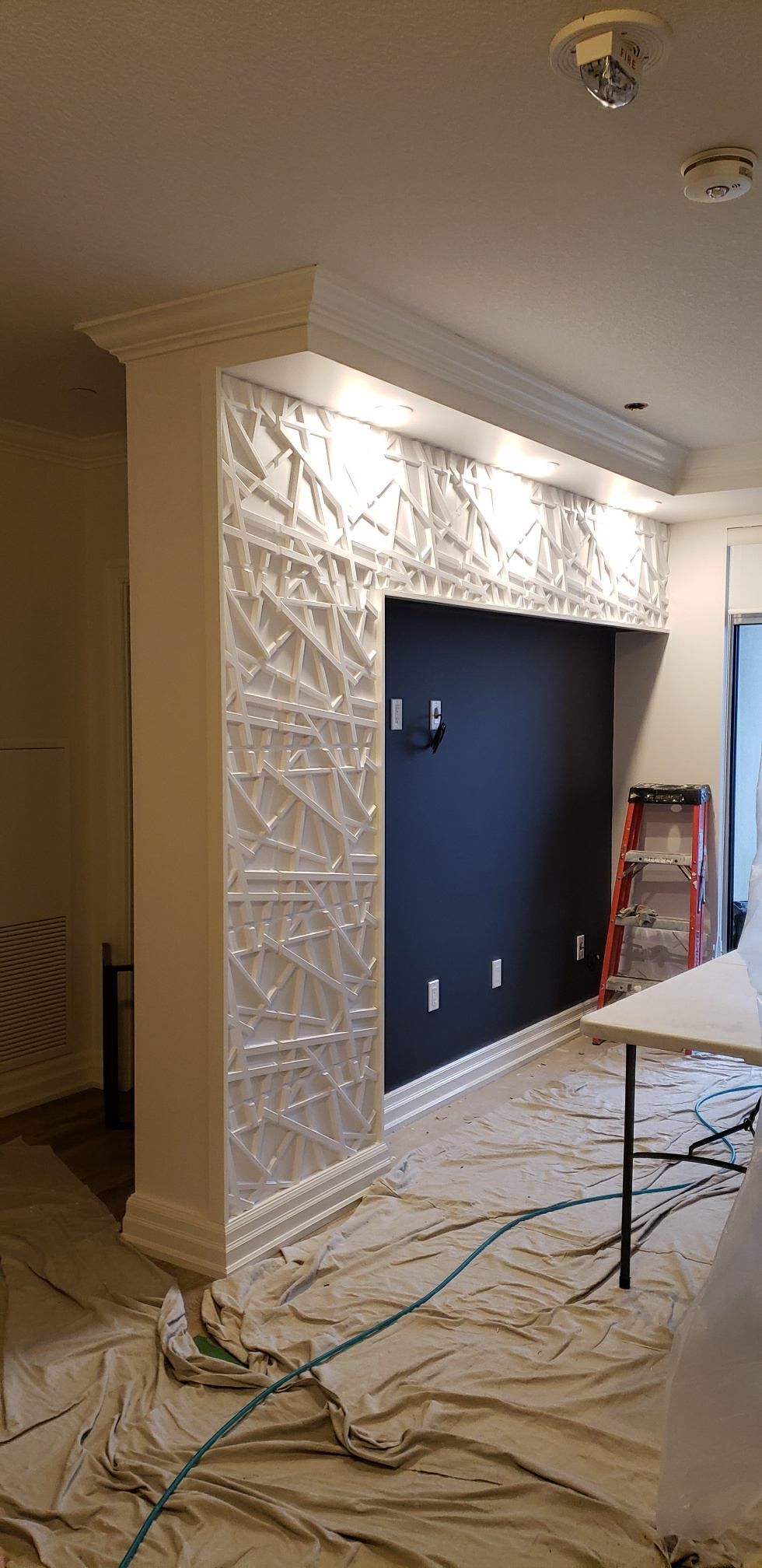 Living room with a white textured fireplace surround under renovation, covered in protective plastic and drop cloths