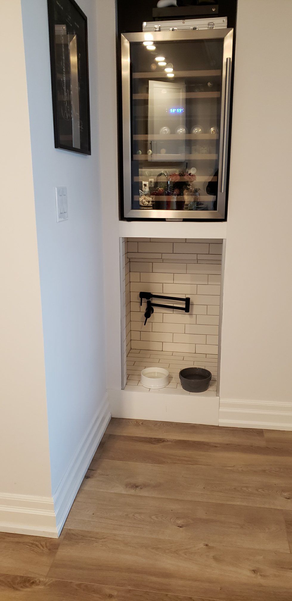 Small built-in alcove with glass-front cabinet, white subway tile, black faucet, and hardwood floor