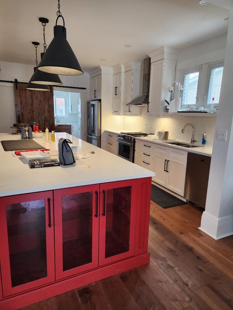 Bright kitchen with white cabinets, red island, hanging pendant lights, and hardwood floors