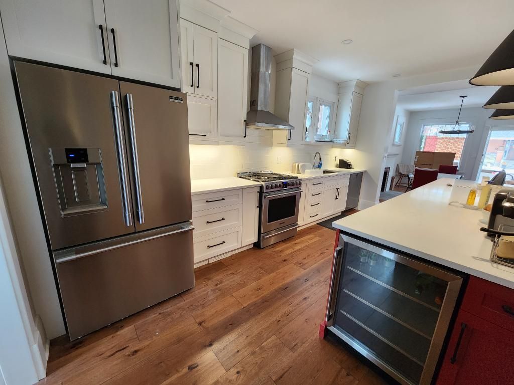 Modern kitchen with stainless steel refrigerator, white cabinets, wood floors, and a large island with sink.
