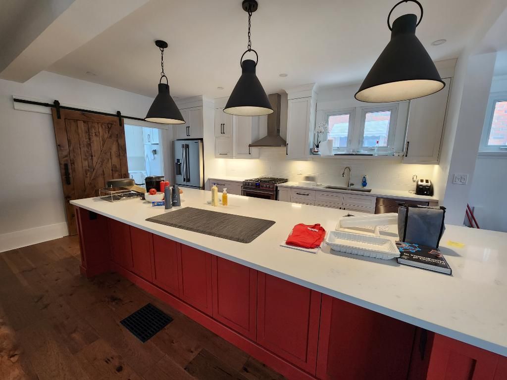 Modern kitchen with red island cabinets, white countertops, black pendant lights, and wooden barn door
