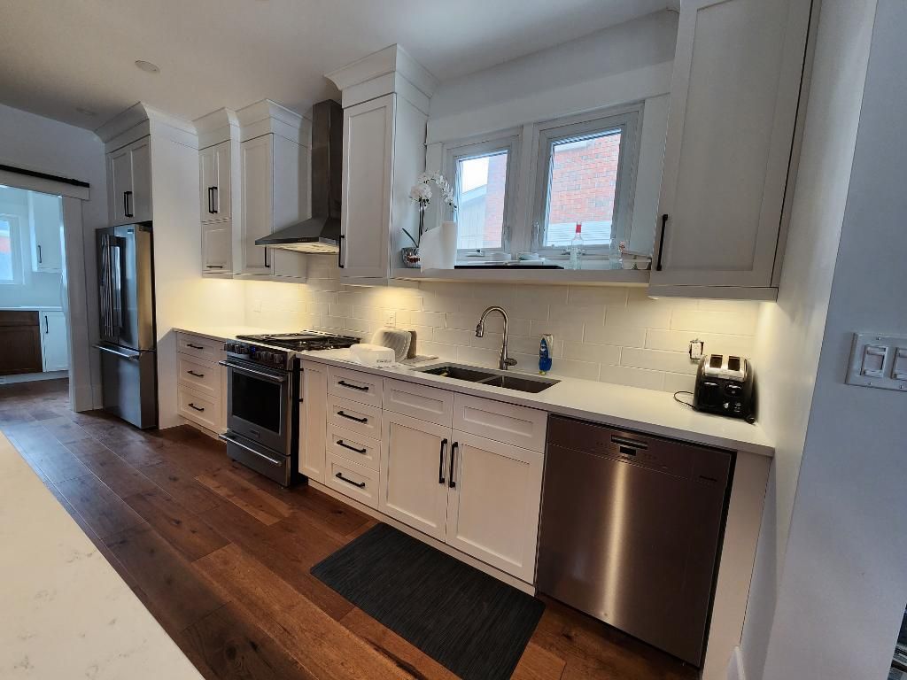 Bright kitchen with white cabinets, stainless appliances, wood floor, and a window over the sink.