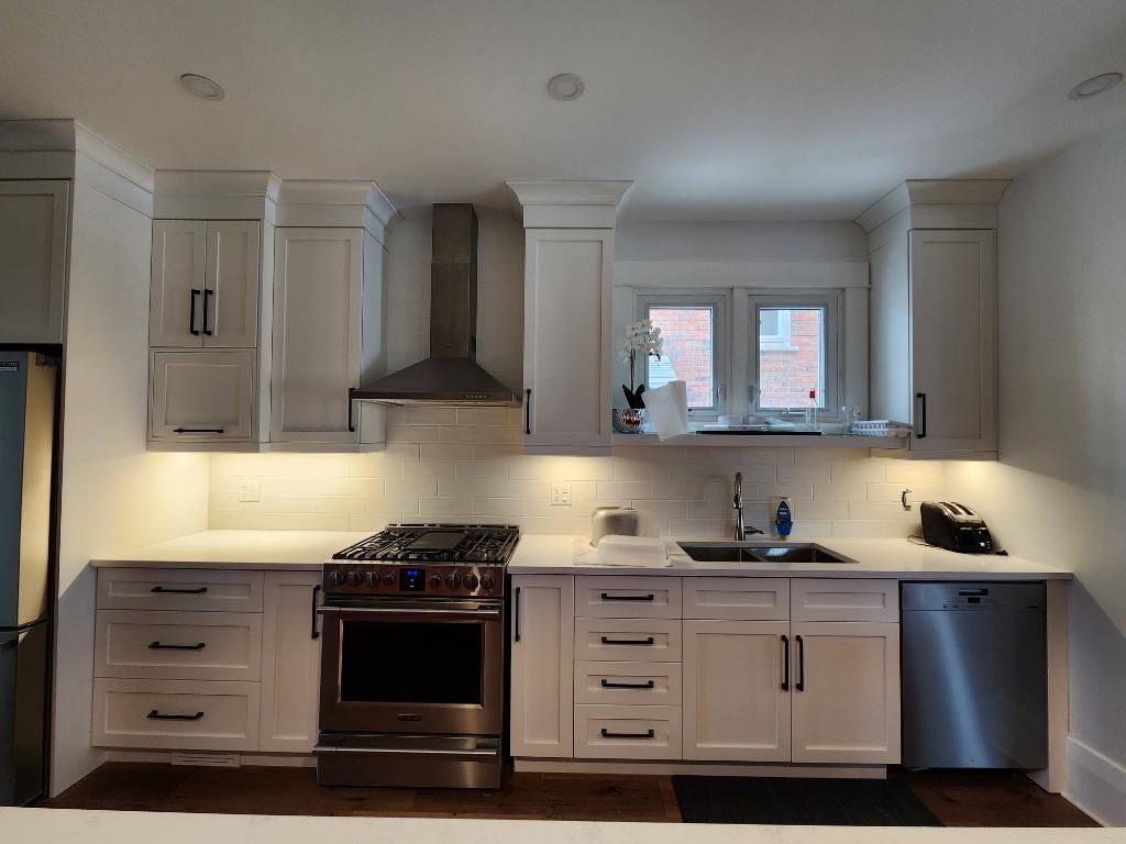 Modern white kitchen with gray cabinets, stainless range, sink under windows, and dishwasher.
