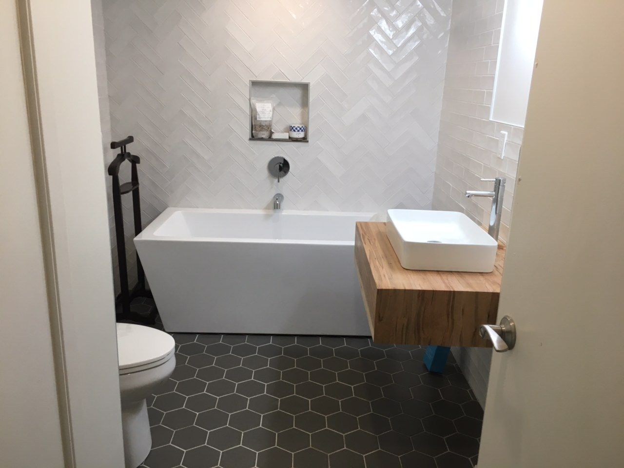 Modern bathroom with freestanding tub, hex tile floor, wall shelf sink, and toilet partially visible
