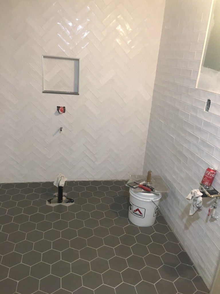 Small tiled bathroom under construction with unfinished walls, hex floor tiles, and plumbing fixtures exposed.