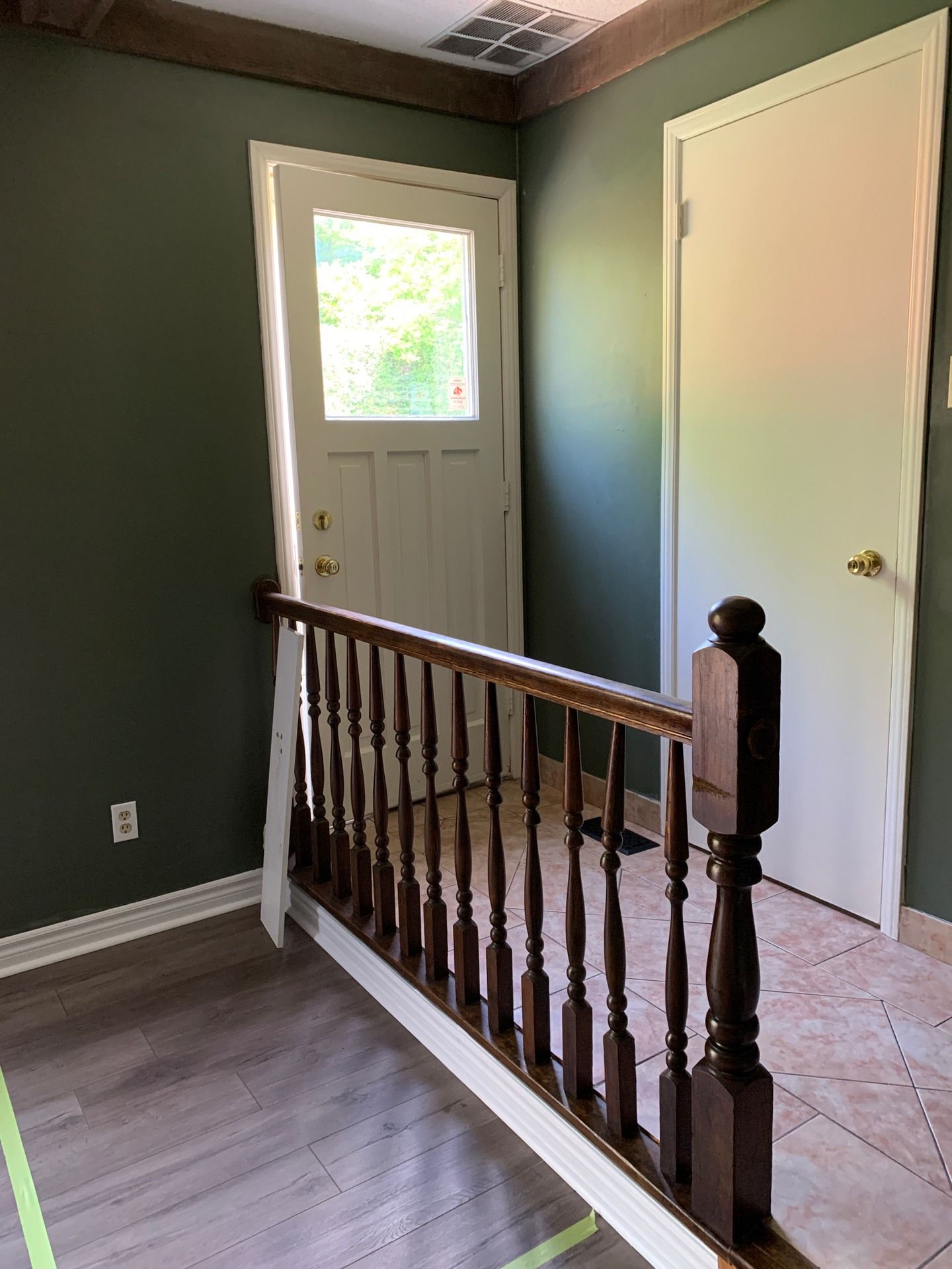 Stair landing with green walls, white front door, closed white closet door, and wood railing.
