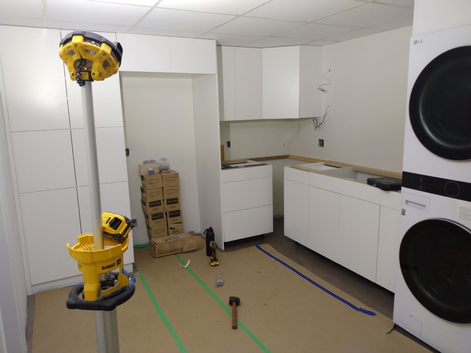 Kitchen with a yellow robot arm and stacked boxes on the floor, beside white cabinets and appliances