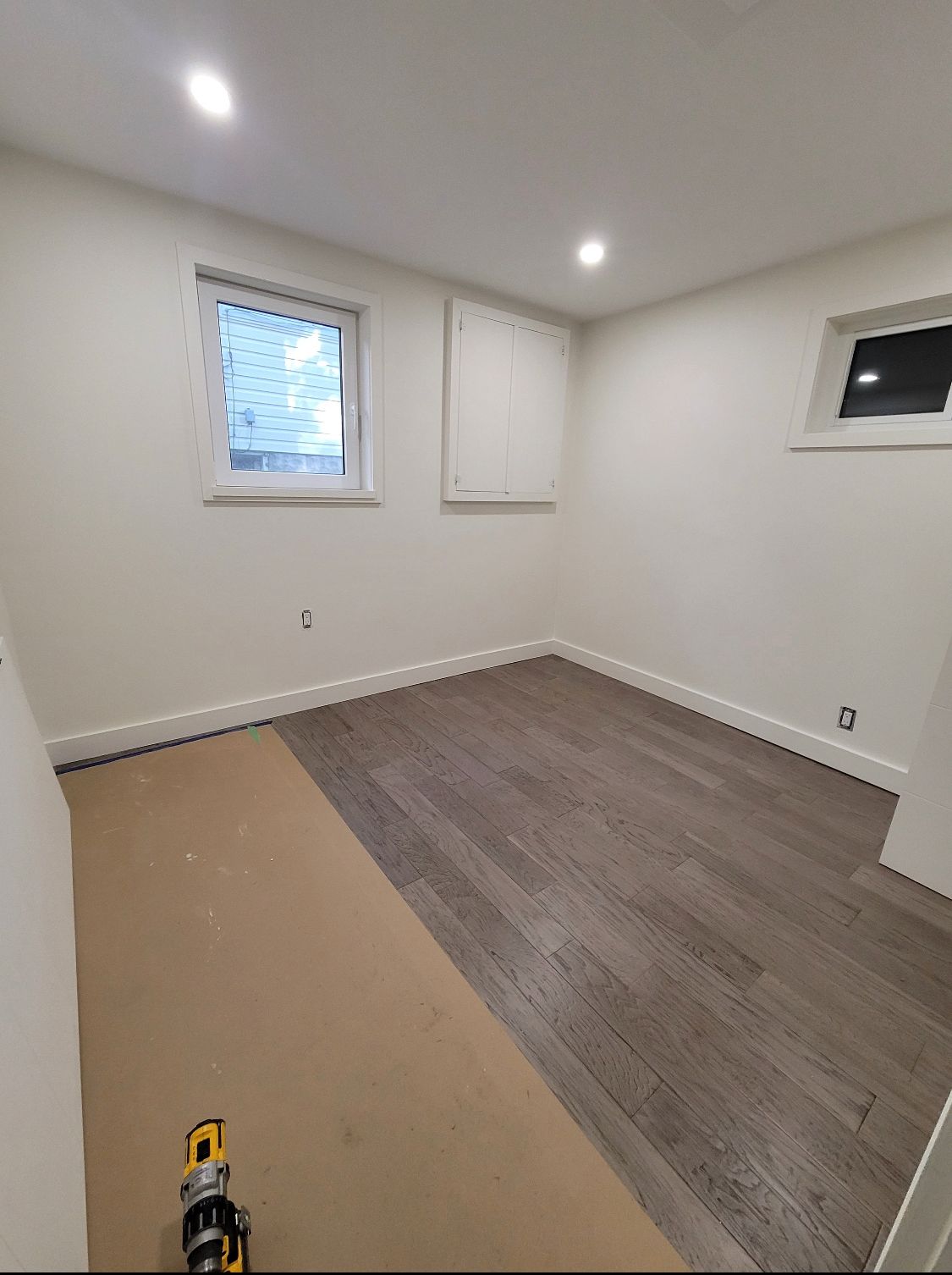 Empty room with white walls, two small windows, and new flooring partially installed.