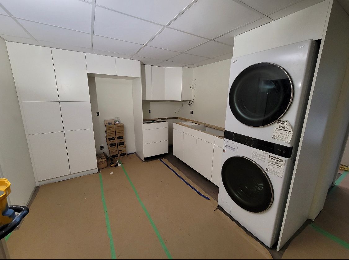 Laundry room with stacked washer and dryer, white cabinets, and cardboard-covered floor