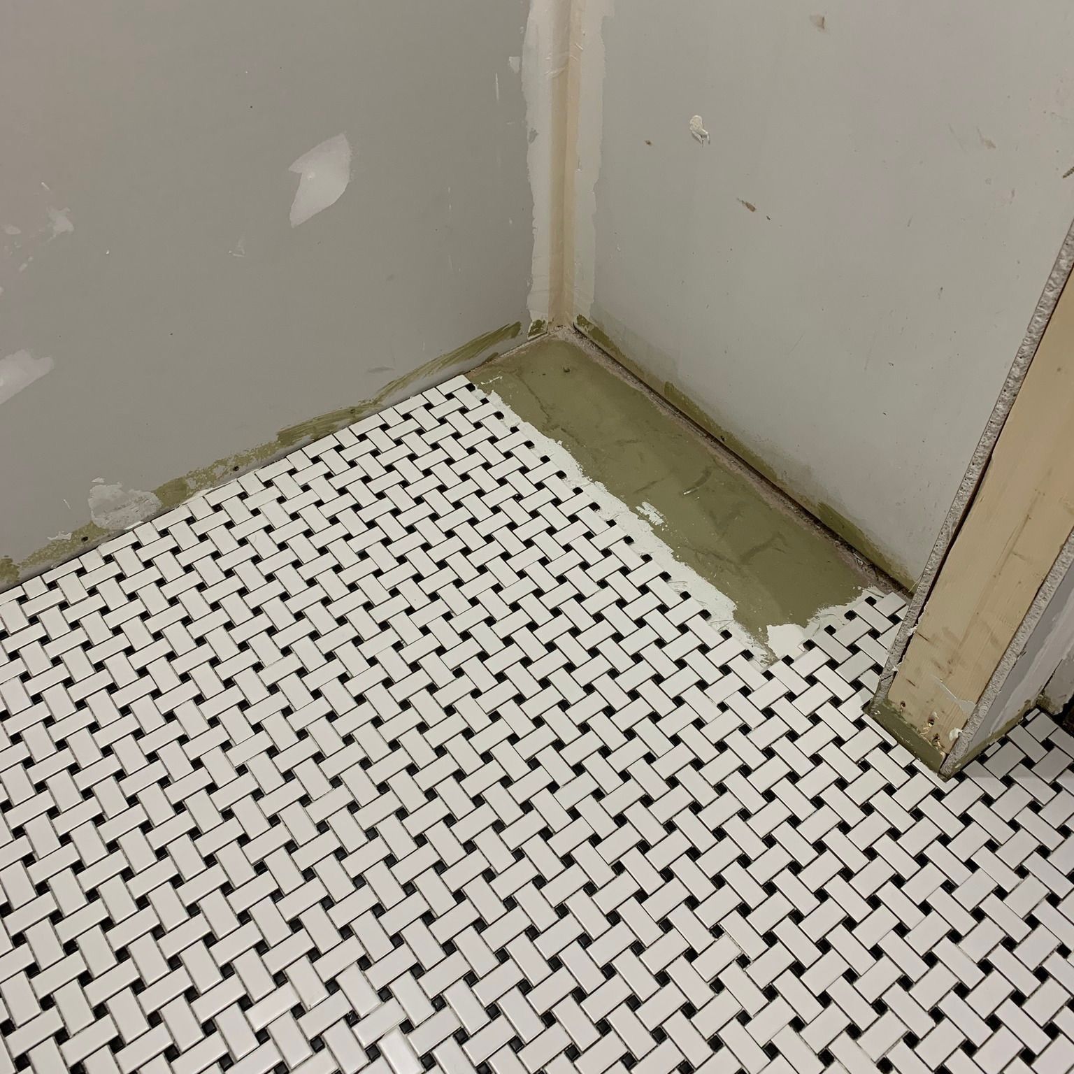 White-and-black patterned floor tiles meet unfinished gray walls and a doorway corner.