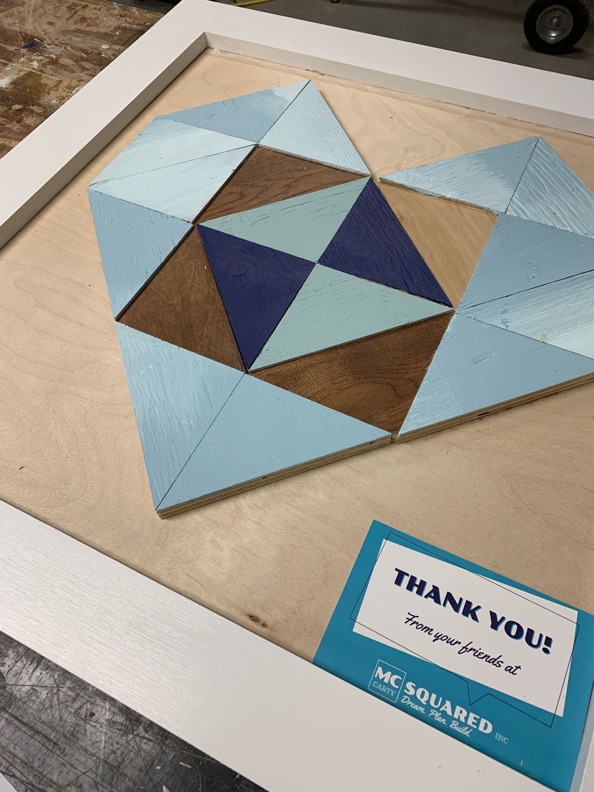 Geometric blue and brown quilt design on a table beside a “THANK YOU” sign