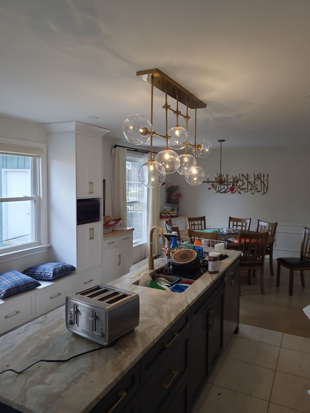 Bright kitchen with island, chandelier lights, and dining table in the background