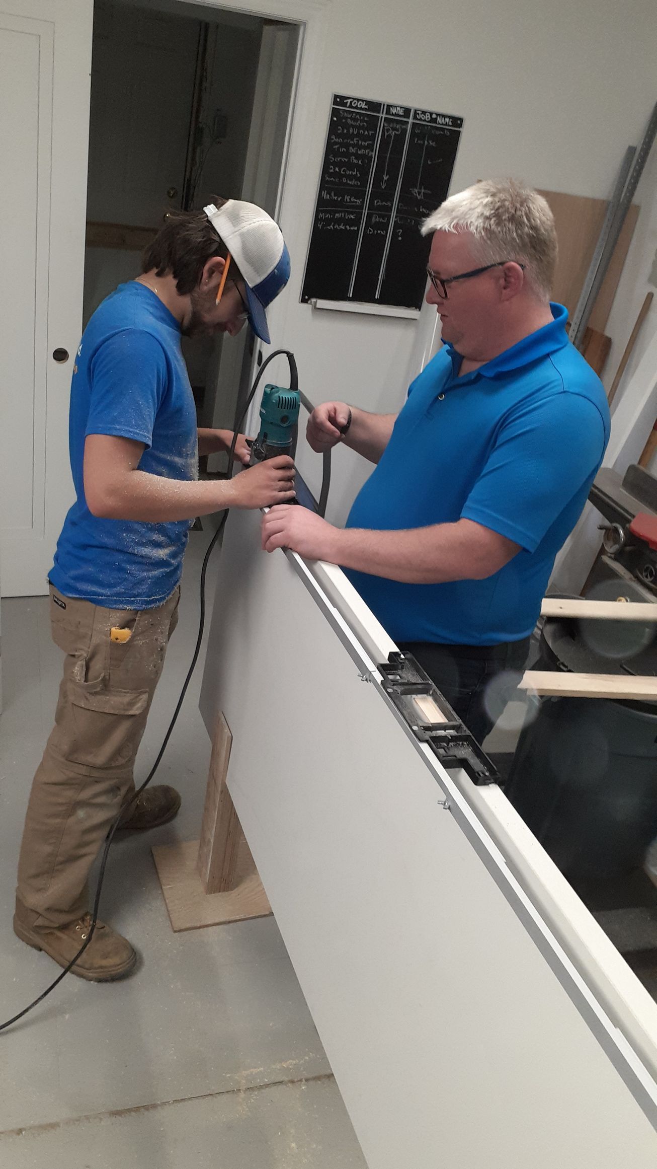 Two men are working on a piece of wood in a room.