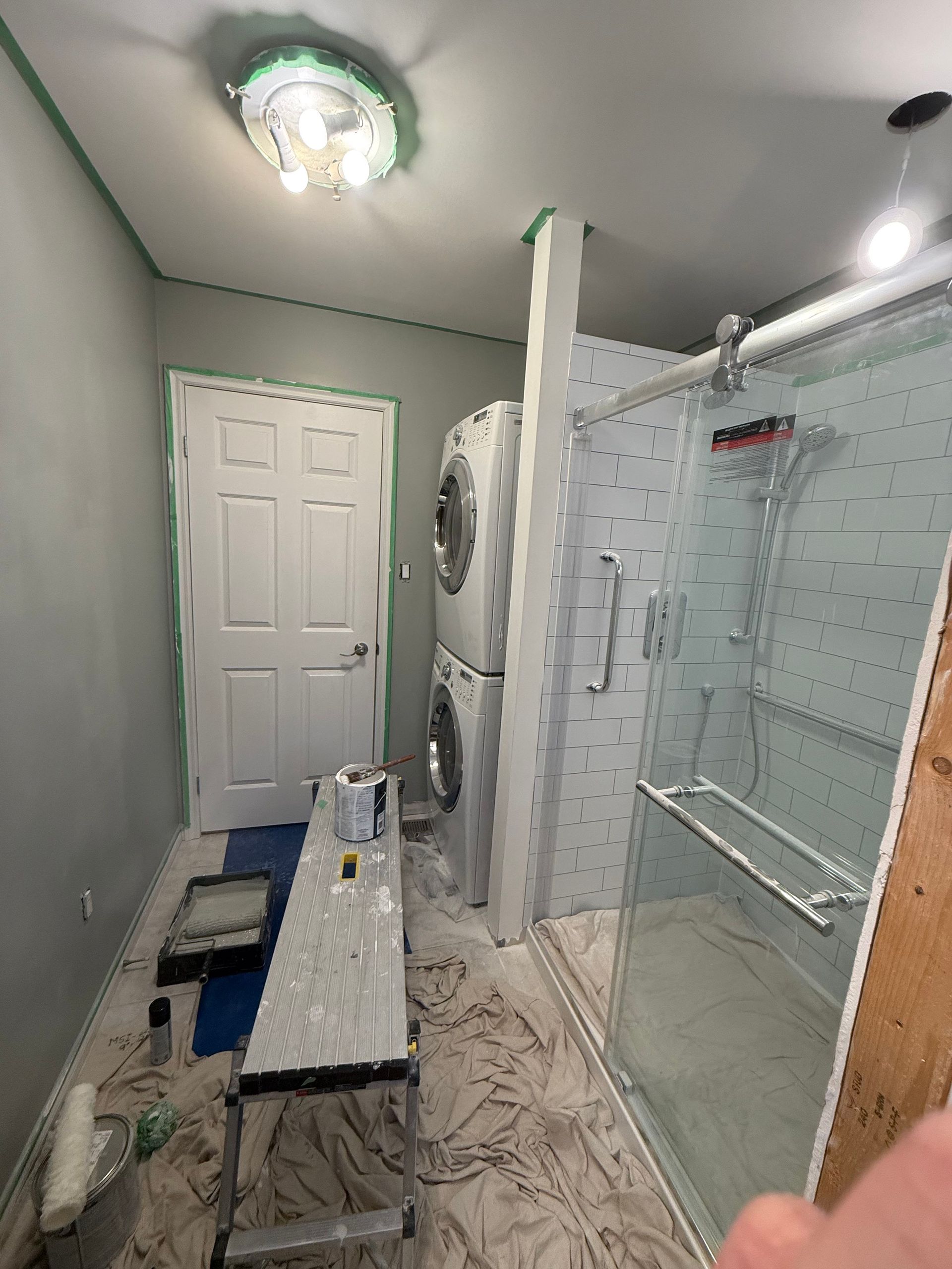 Narrow bathroom with shower stall, toilet, sink, and bench; white walls and glass doors.
