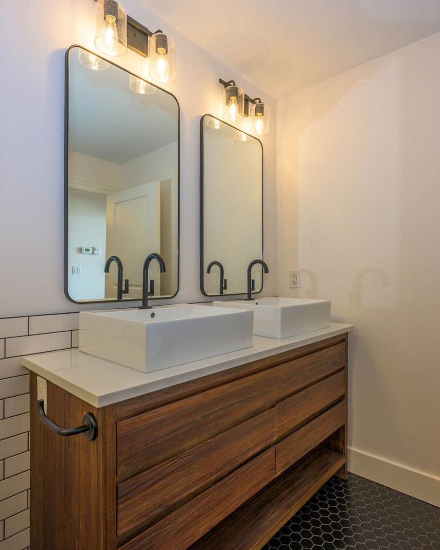 Modern bathroom vanity with two mirrors, vessel sinks, and wall sconces on a wood cabinet.