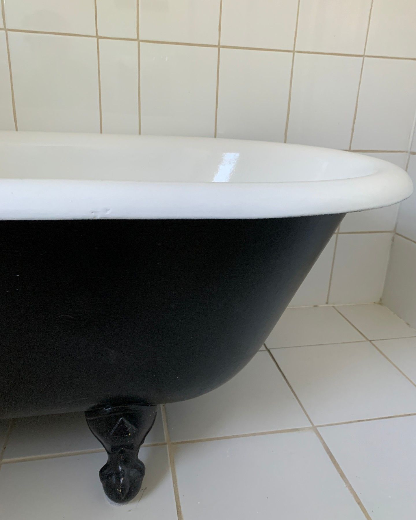 Black clawfoot bathtub with a white rim in a tiled bathroom.