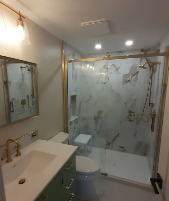 Modern bathroom with glass shower, white marble-look tile, vanity sink, mirror, and toilet.
