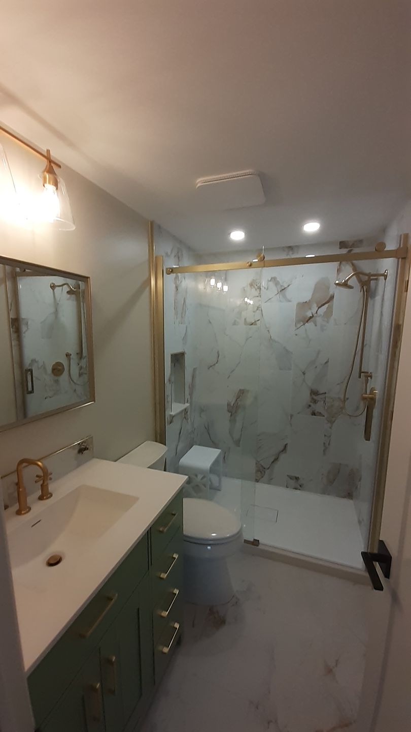 Modern bathroom with marble shower, white toilet, green vanity, and wall mirror