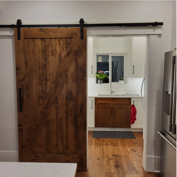 Sliding barn door opens to a kitchen and bathroom vanity with wood cabinets and white counters.