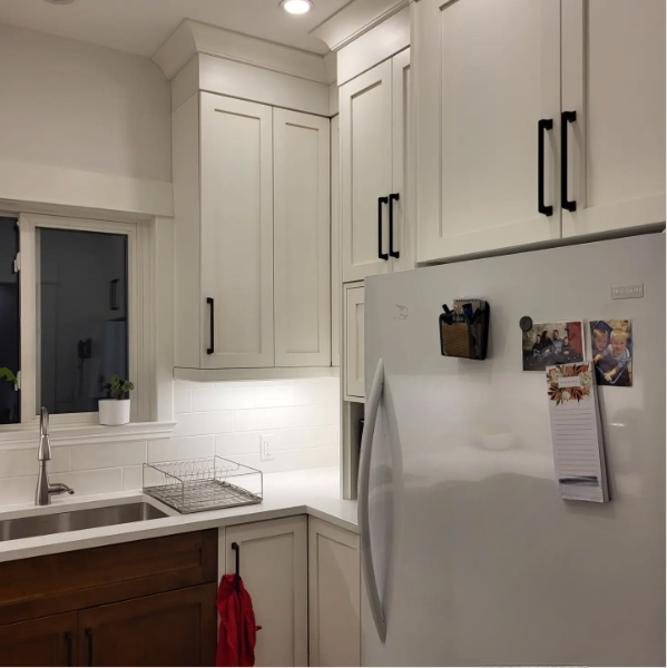 Modern white kitchen with cabinets, sink, fridge, and under-cabinet lighting, viewed at night