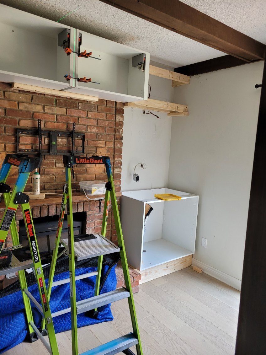 Partially renovated room with exposed brick wall, white cabinets, a ladder, and a small white shelf unit