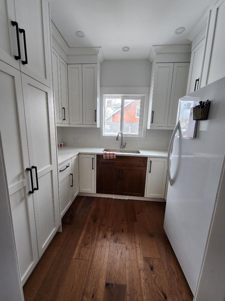 A kitchen with white cabinets and wooden floors and a refrigerator.
