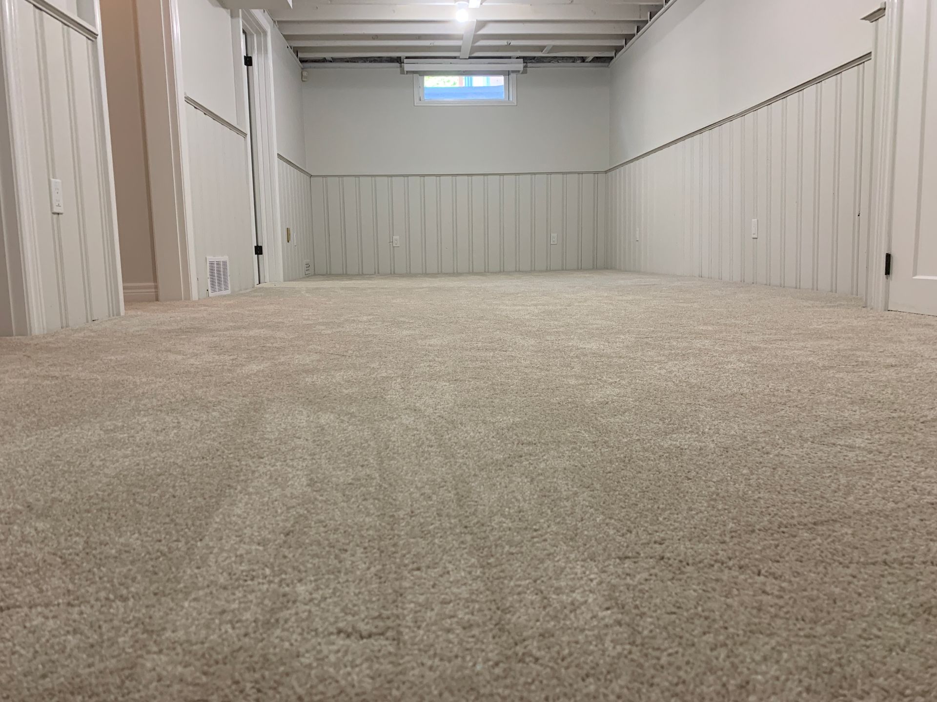 An empty basement with a carpeted floor and white walls.