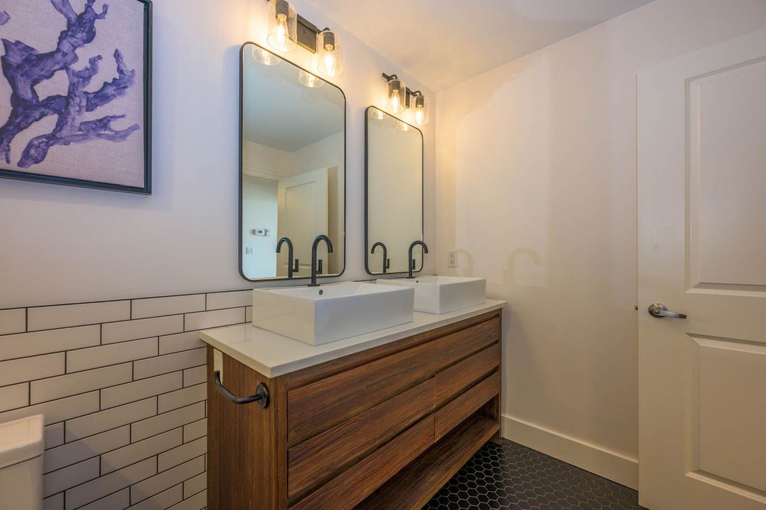 A modern double-sink bathroom vanity with wood drawers, white subway tile walls, and two rectangular mirrors.