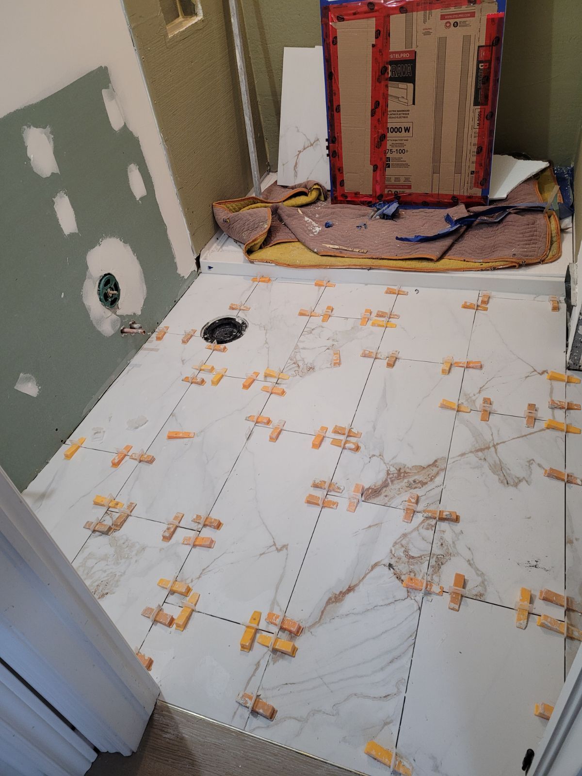 A bathroom under construction with tiles on the floor and a box on the wall.