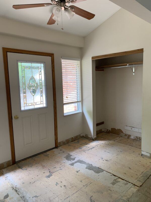 Small empty room with a front door, window, open closet, and worn floor under a ceiling fan.