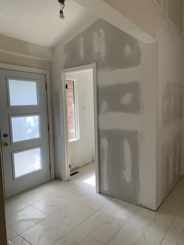 Unfinished interior hallway with drywall patching, white tile floor, and a door to a small room.