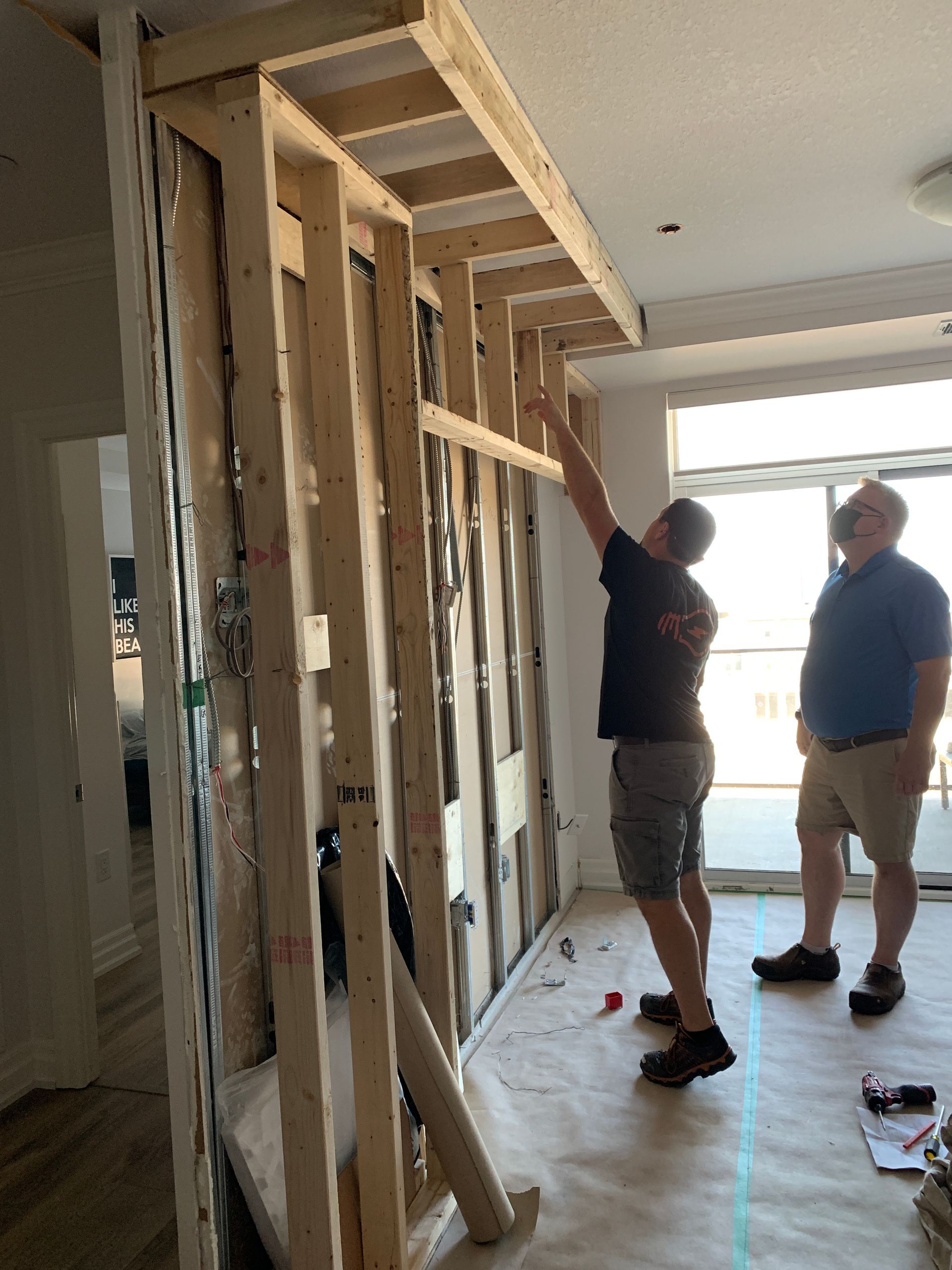 Two men are working on a wooden frame in a room.